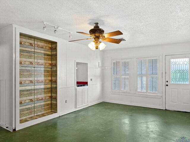 interior space with a textured ceiling, finished concrete floors, track lighting, ceiling fan, and visible vents