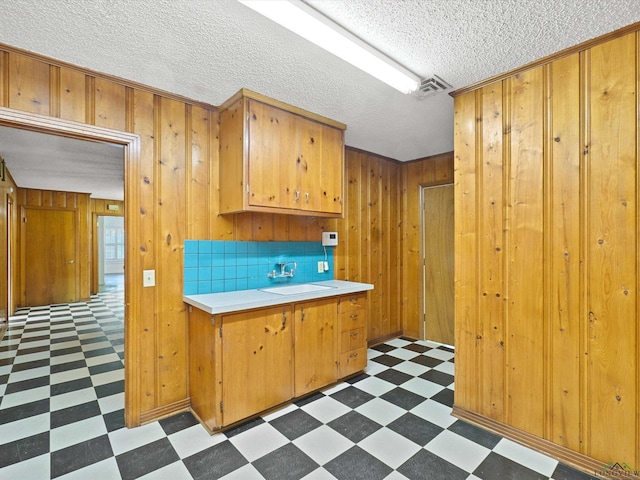 kitchen featuring dark floors, wood walls, light countertops, visible vents, and a sink