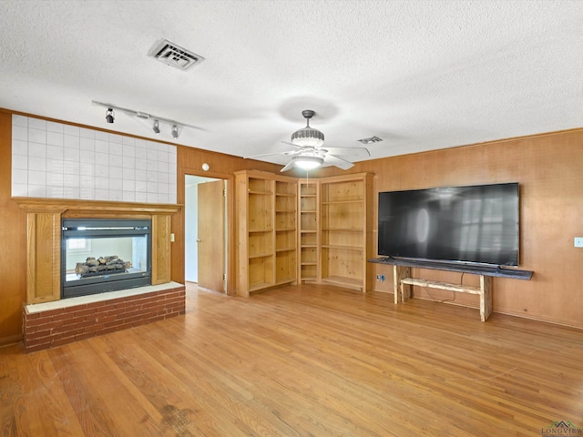 unfurnished living room featuring a glass covered fireplace, wood finished floors, a textured ceiling, and visible vents