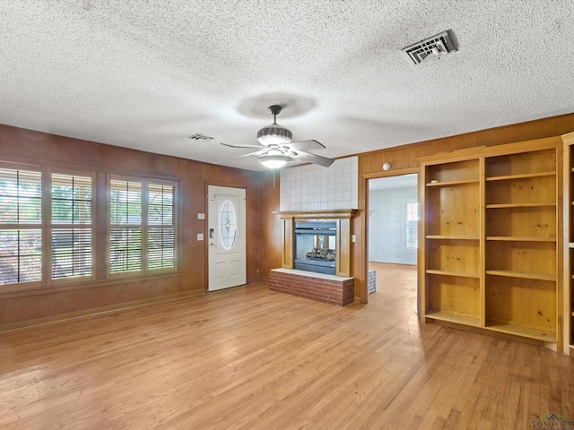 unfurnished living room with wooden walls, a ceiling fan, light wood-style floors, and visible vents