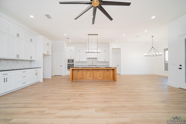 kitchen with decorative light fixtures, a spacious island, oven, light wood-type flooring, and white cabinets