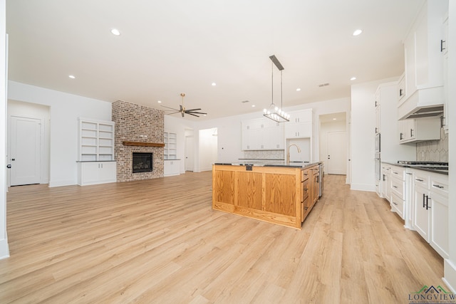 kitchen with hanging light fixtures, white cabinets, a kitchen island with sink, and decorative backsplash