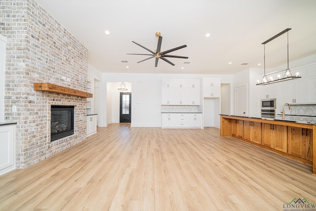 kitchen featuring white cabinetry, a brick fireplace, appliances with stainless steel finishes, backsplash, and hanging light fixtures