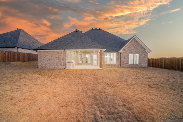 back house at dusk with a lawn and a patio