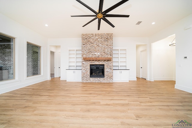 unfurnished living room featuring a brick fireplace, built in features, light hardwood / wood-style flooring, and ceiling fan