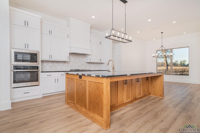 kitchen featuring decorative light fixtures, backsplash, black appliances, a large island, and white cabinets