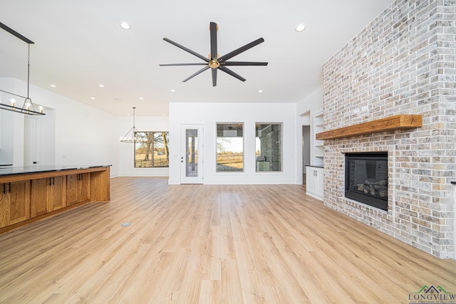 unfurnished living room with a brick fireplace, light hardwood / wood-style floors, and ceiling fan with notable chandelier