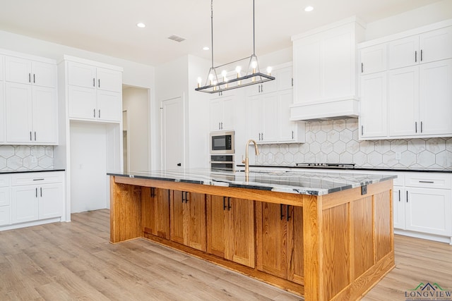 kitchen featuring stainless steel appliances, backsplash, a center island with sink, and decorative light fixtures