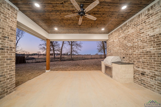 patio terrace at dusk featuring ceiling fan and exterior kitchen