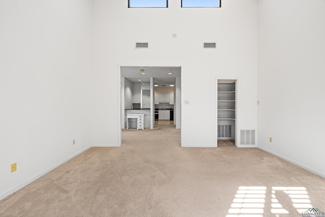 unfurnished living room with light colored carpet and a towering ceiling