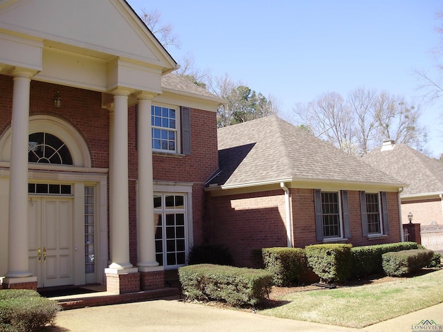 exterior space featuring brick siding and a shingled roof