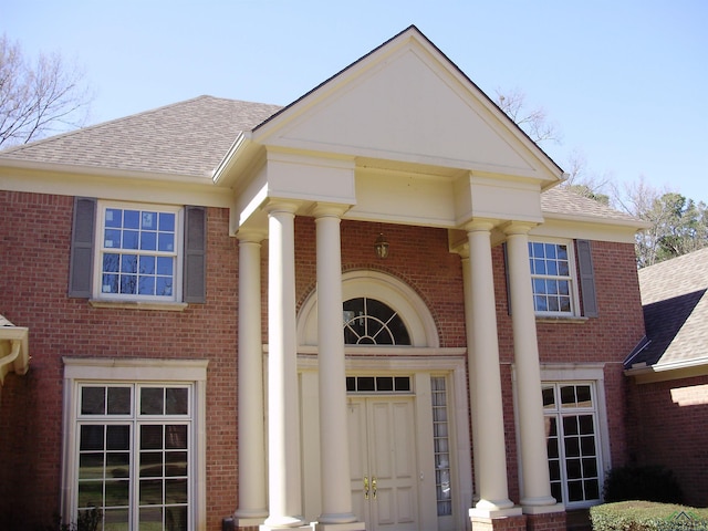 property entrance featuring brick siding and a shingled roof