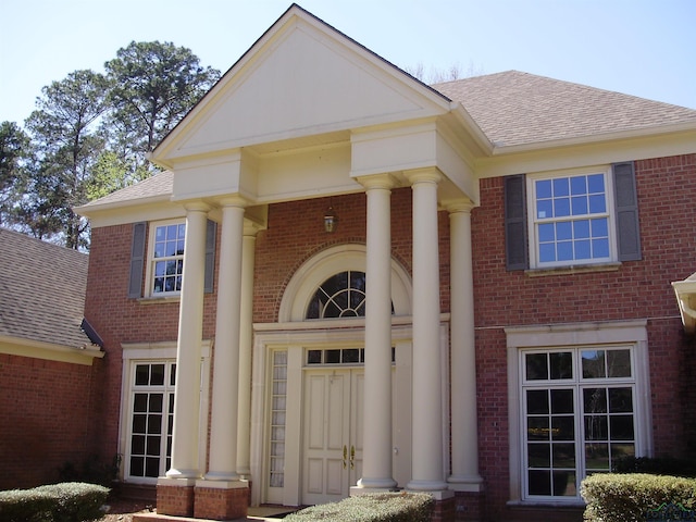 view of exterior entry featuring brick siding and a shingled roof