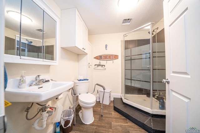 full bathroom featuring a stall shower, toilet, wood finished floors, a textured ceiling, and a sink