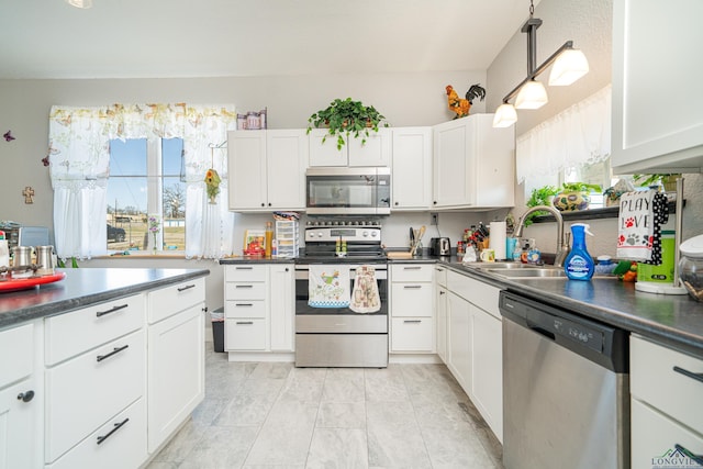 kitchen with dark countertops, stainless steel appliances, white cabinetry, pendant lighting, and a sink