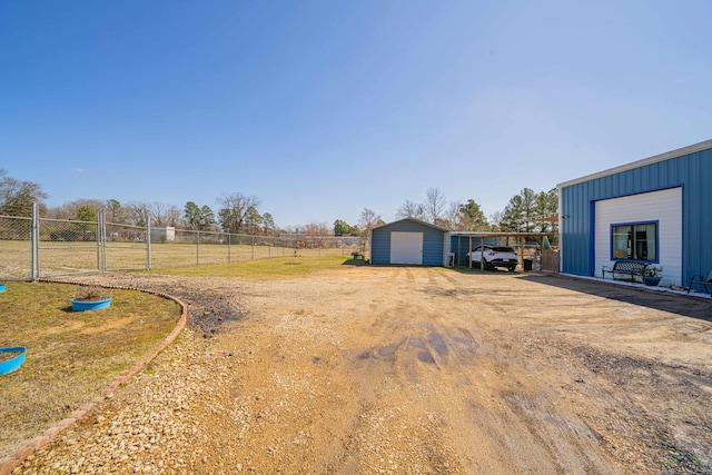 view of yard featuring driveway, a pole building, fence, and an outbuilding