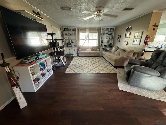 living room featuring built in shelves, ceiling fan, dark hardwood / wood-style flooring, wood walls, and a textured ceiling