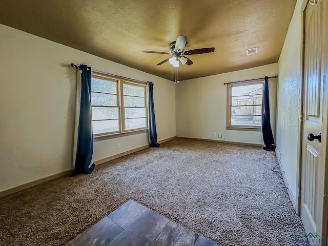 empty room with carpet, baseboards, a textured ceiling, visible vents, and a ceiling fan