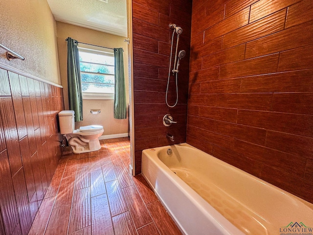full bath with a textured ceiling, wood walls, wood finished floors, toilet, and shower / washtub combination