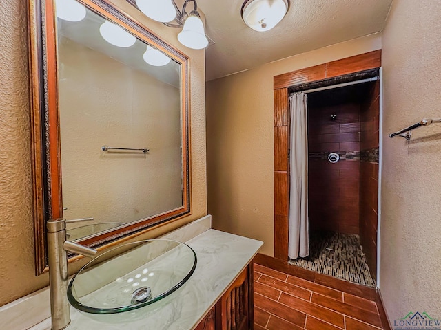 full bath with a tile shower, a textured wall, and wood finish floors