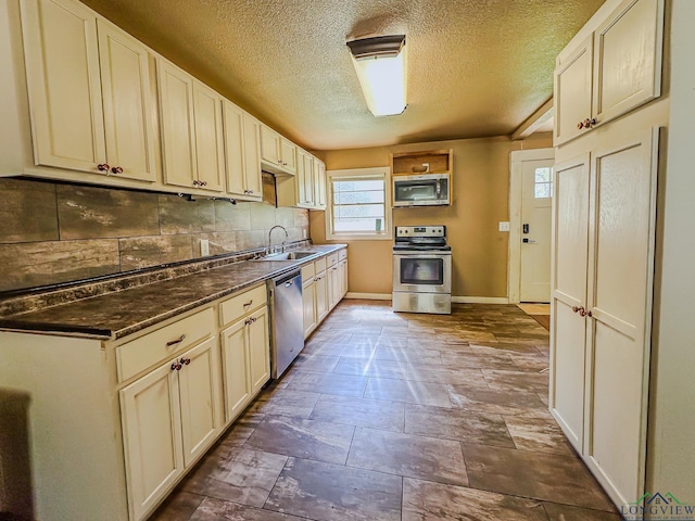 kitchen with a sink, backsplash, appliances with stainless steel finishes, baseboards, and dark countertops