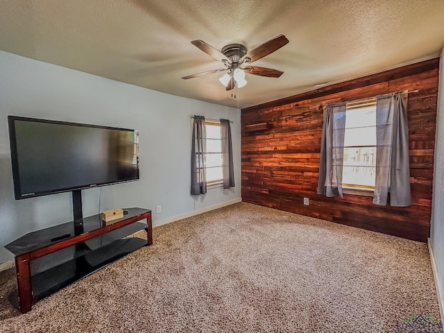 unfurnished living room featuring a wealth of natural light, wooden walls, carpet, and a textured ceiling