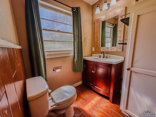 bathroom featuring baseboards, toilet, wood finished floors, vanity, and a textured wall