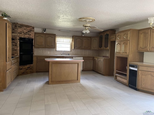 kitchen with ceiling fan, sink, backsplash, black double oven, and a kitchen island