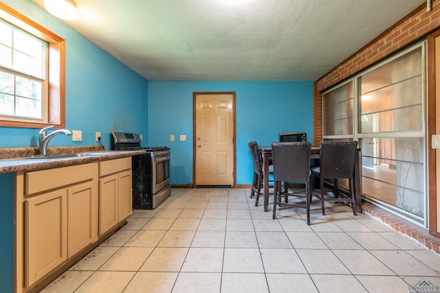 kitchen with brick wall, stainless steel gas range, a textured ceiling, sink, and light tile patterned floors