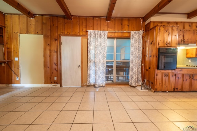 interior space featuring beam ceiling, black oven, wooden walls, and light tile patterned flooring