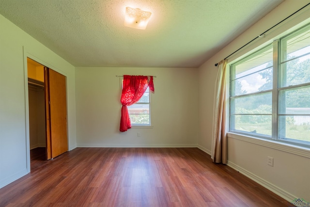 unfurnished bedroom featuring multiple windows, a closet, dark wood-type flooring, and a textured ceiling