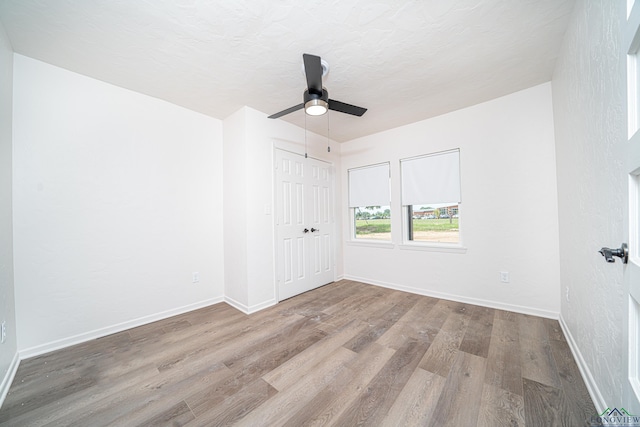 empty room with ceiling fan, light wood-type flooring, and a textured ceiling