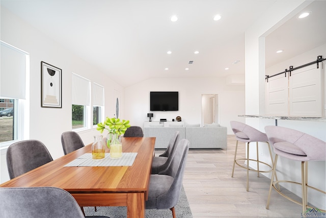 dining room featuring a barn door, lofted ceiling, and light hardwood / wood-style flooring