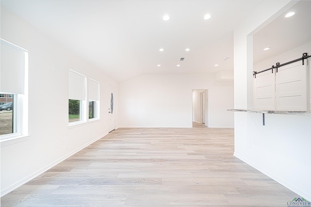 spare room with light wood-type flooring, a barn door, and lofted ceiling