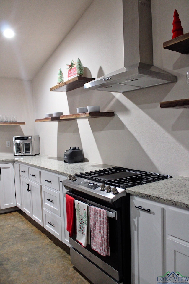 kitchen with wall chimney range hood, light stone countertops, stainless steel range with gas stovetop, and white cabinets