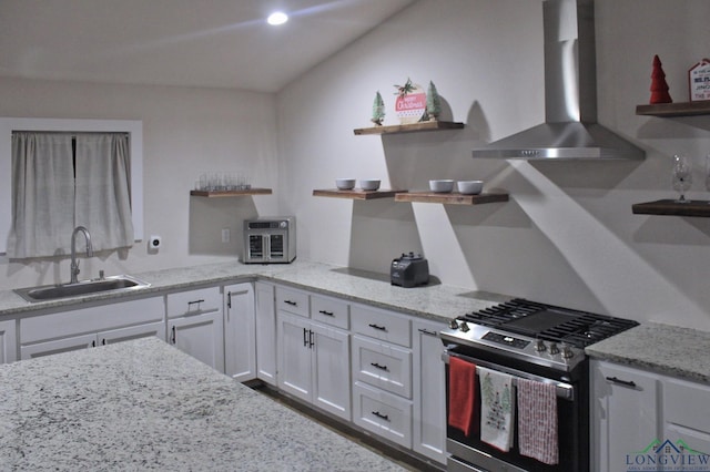 kitchen with stainless steel range with gas cooktop, sink, white cabinets, light stone countertops, and wall chimney range hood