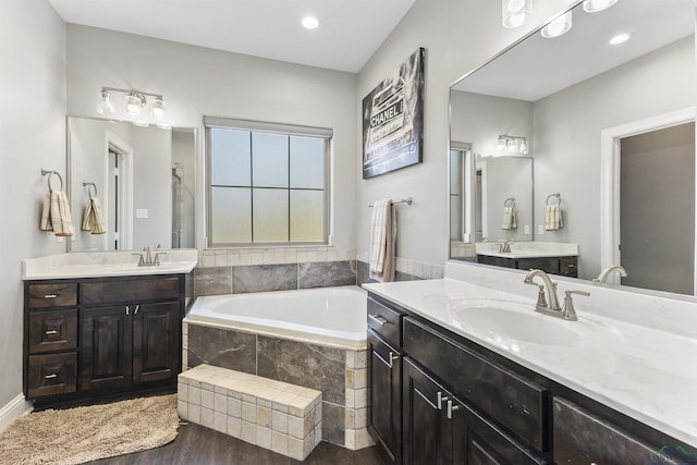 full bathroom featuring wood finished floors, two vanities, recessed lighting, a sink, and a garden tub