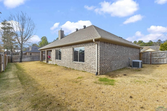 rear view of house featuring brick siding, central AC unit, a chimney, and a yard