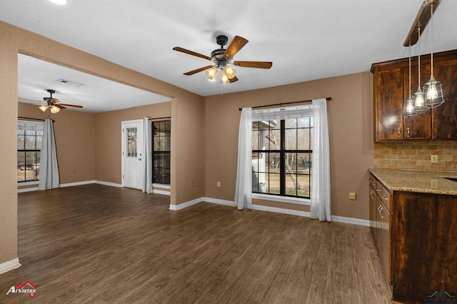 unfurnished living room with plenty of natural light, visible vents, dark wood finished floors, and baseboards