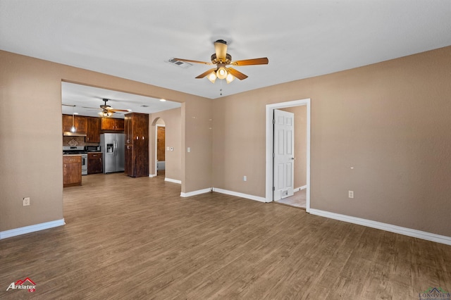 unfurnished living room with arched walkways, ceiling fan, dark wood-style floors, and baseboards