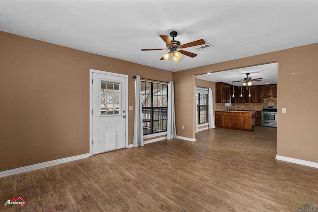 unfurnished living room with baseboards, visible vents, and wood finished floors