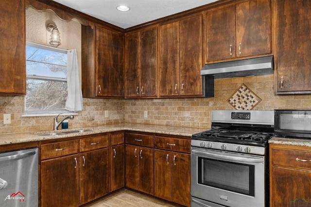 kitchen with light stone counters, backsplash, appliances with stainless steel finishes, a sink, and under cabinet range hood