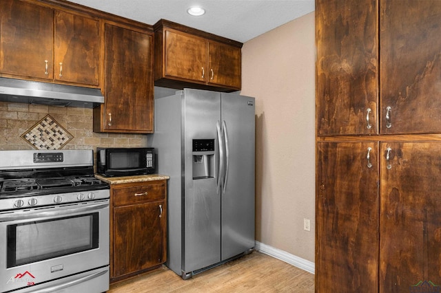 kitchen with stainless steel appliances, decorative backsplash, light wood-type flooring, under cabinet range hood, and baseboards