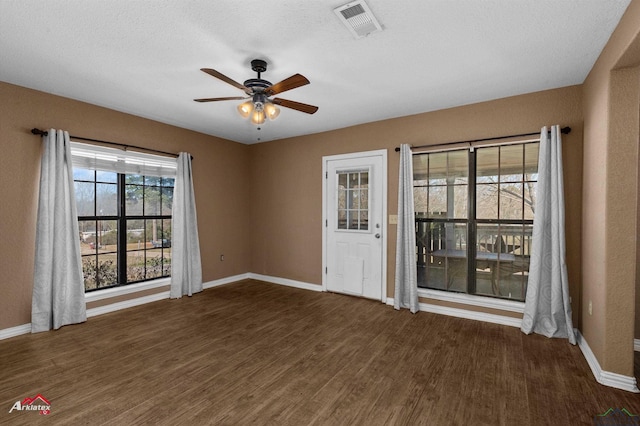 spare room with a textured ceiling, visible vents, baseboards, a ceiling fan, and dark wood-style floors