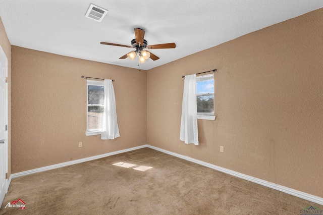 carpeted empty room featuring a ceiling fan, visible vents, and baseboards