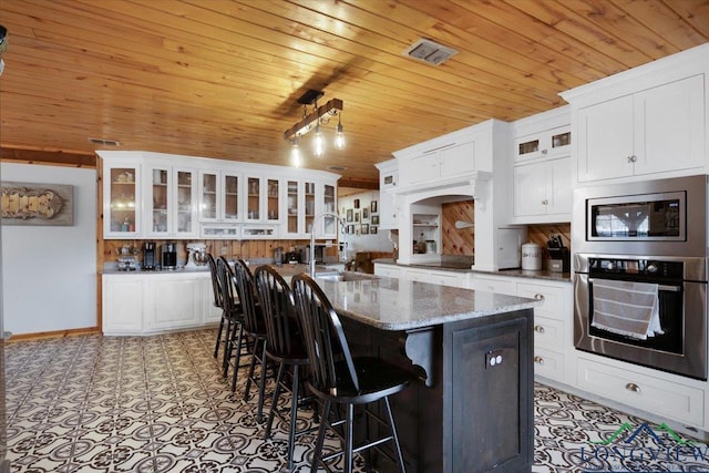 kitchen with a kitchen island with sink, white cabinets, stone counters, and appliances with stainless steel finishes