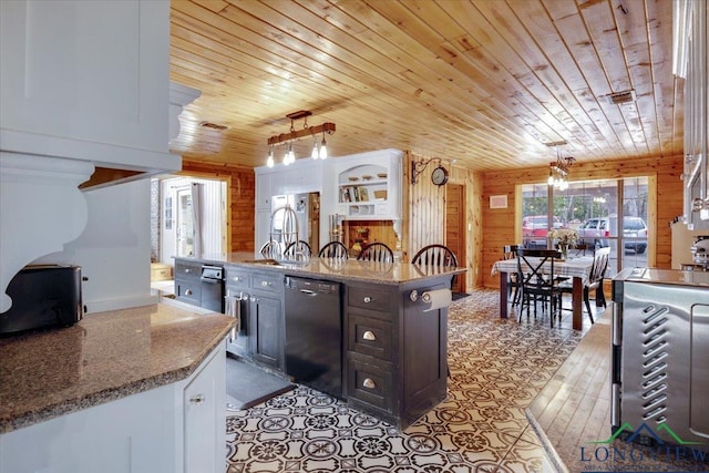 kitchen with light stone counters, decorative light fixtures, black dishwasher, and wood walls