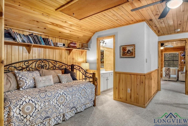 carpeted bedroom featuring lofted ceiling, wood ceiling, wooden walls, and ensuite bath