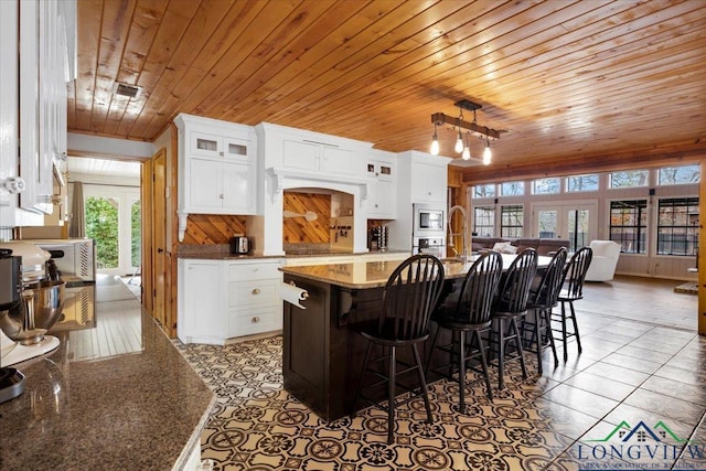 kitchen featuring a breakfast bar, appliances with stainless steel finishes, an island with sink, white cabinets, and stone countertops