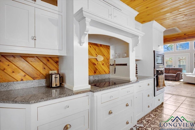 kitchen with light tile patterned floors, wood ceiling, appliances with stainless steel finishes, white cabinetry, and dark stone countertops